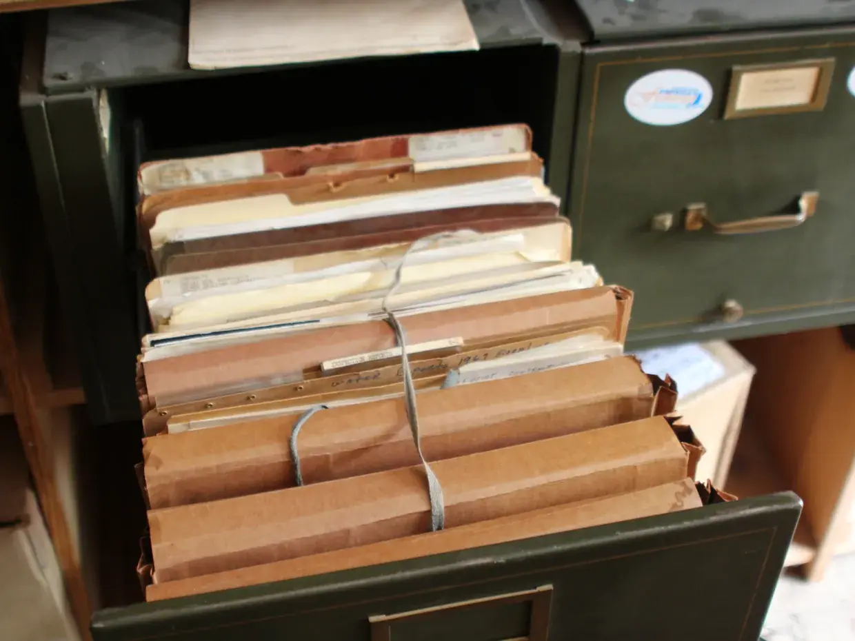 An opened steel drawer packed with bundled paper files tied with string
